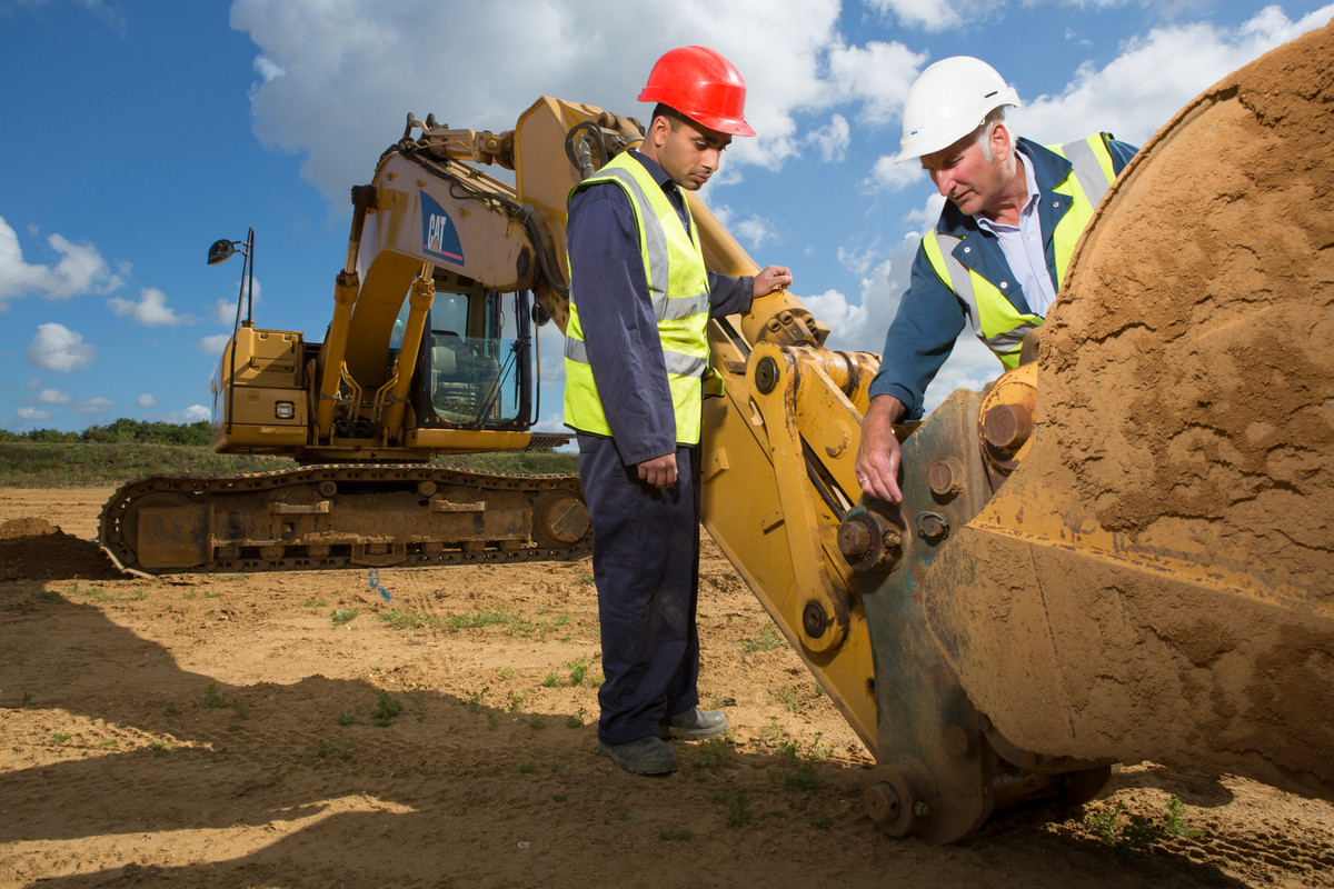 Image of two men with hard hats and high vis jackets on a construction site, inspecting an Excavator