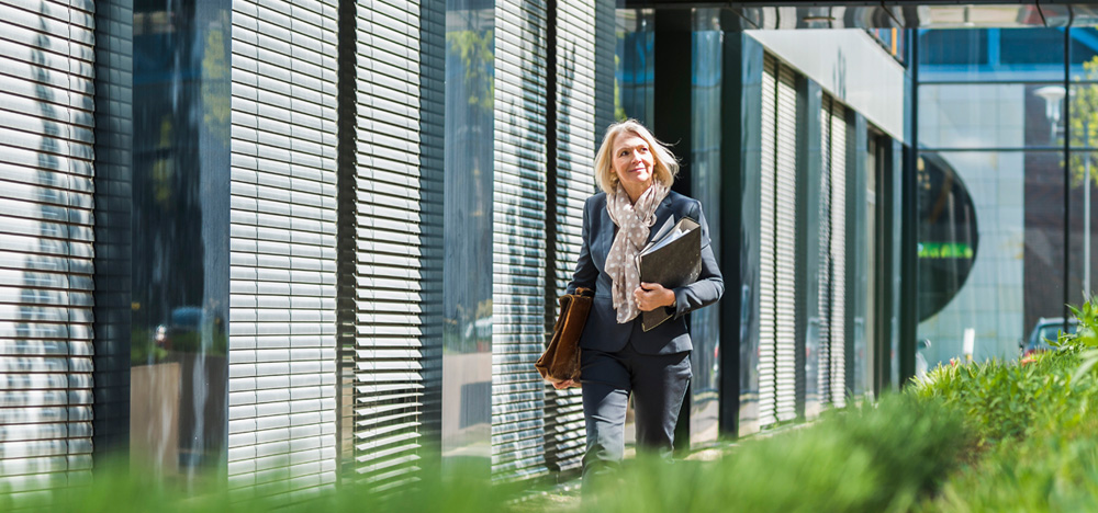 Image of a woman walking past a building carrying some folders 