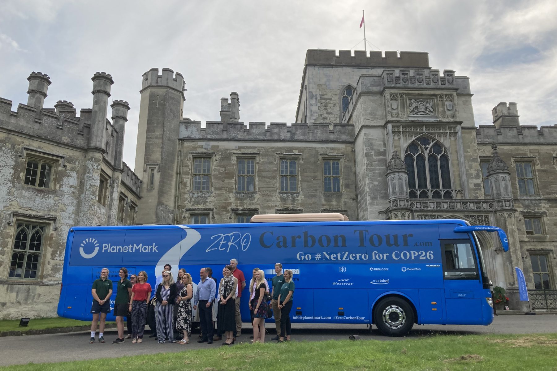 Image showing the a blue Coach with Carbon Tour branding. There are 18 people stood in front of the coach